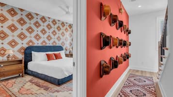 A hotel room with a patterned wall, a bed with white linens, a blue headboard, a nightstand, a lamp, and a wall-mounted shoe rack.