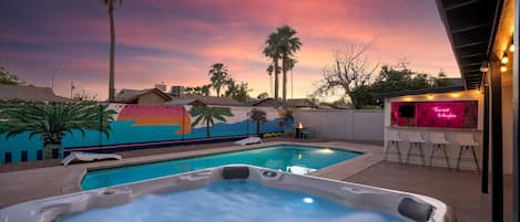 A hot tub with a pool, a bar area with neon lights, and a sunset sky.