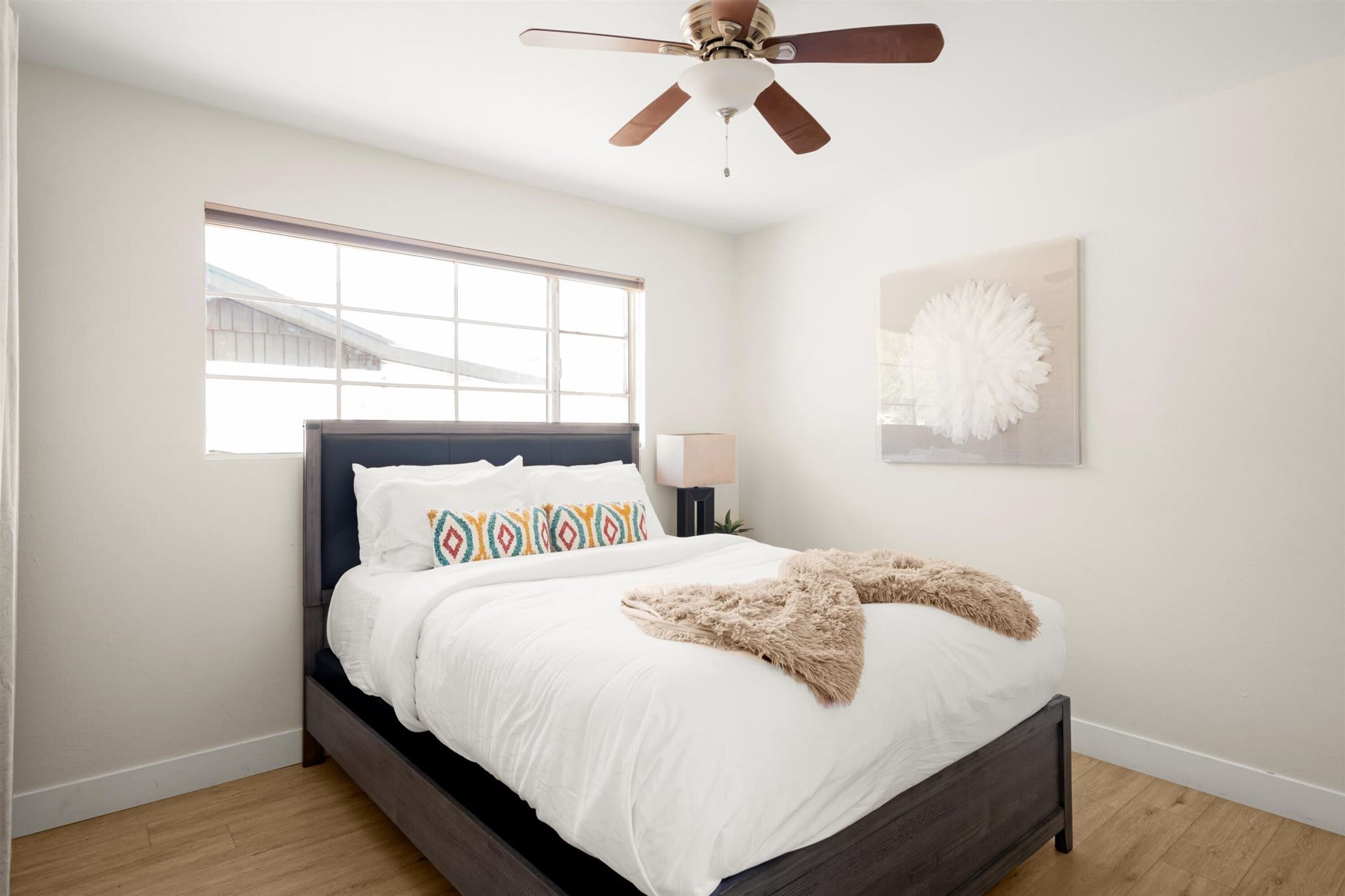 Ein Schlafzimmer mit Bett, Deckenventilator, Fenster und einem Wandbild.