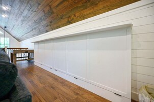 Una habitación con suelo de madera, pared blanca con un banco empotrado y techo inclinado.