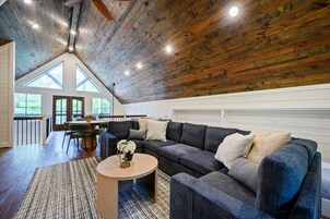 Un loft amplio con techo alto, un sofá seccional gris oscuro, una mesa de centro redonda y vistas al exterior a través de amplios ventanales.