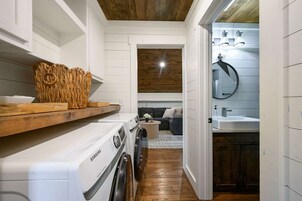 A laundry area with a washing machine, a drying rack, and a wooden shelf.