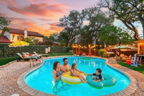 A swimming pool with a curved edge, surrounded by a wooden deck and a hedge. - Elegant Escape Sleeps 14 Games Pool Fire Pit (San Antonio)