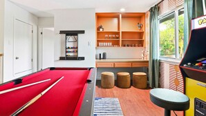 A pool table with cues, a billiards rack, and stools in a room with a window, shelves with glasses, and a pool table. - Elegant Escape Sleeps 14 Games Pool Fire Pit (San Antonio)