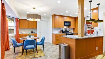 A compact kitchen with a dining area, featuring wooden cabinets, a microwave, a stove, and a small island with a sink.