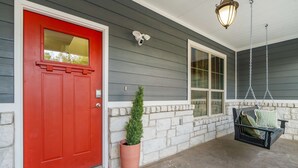 A red door, a potted plant, a stone wall, a hanging light fixture, and a porch swing. - Austin Compound Pickleball Pool Sauna (Austin)