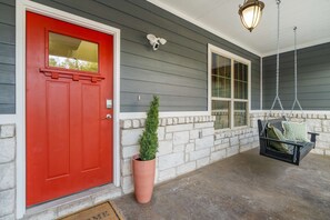 A red door, a potted plant, a stone wall, a hanging light fixture, and a porch swing. - Austin Compound Pickleball Pool Sauna (Austin)