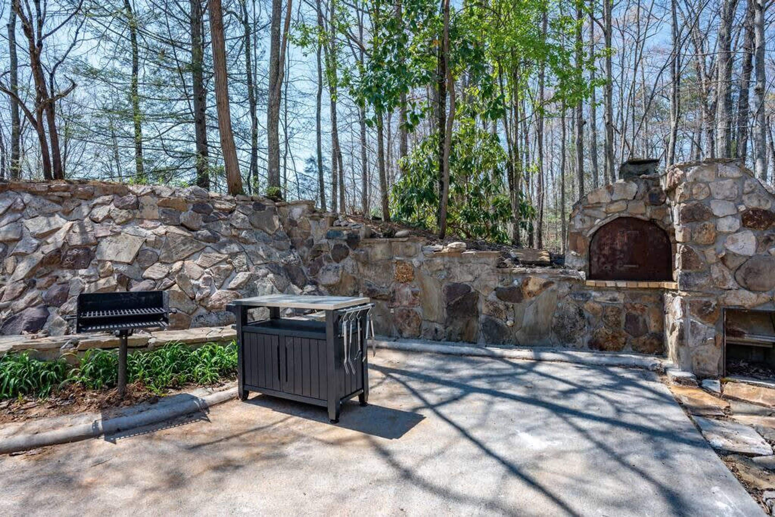 Eine Steinmauer mit Grill und Steinofen, umgeben von Bäumen.