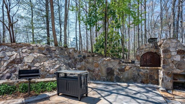 A stone wall with a grill and a stone oven, surrounded by trees. - Mountain View - Rooftop Patio - Theater - Games (Gatlinburg)