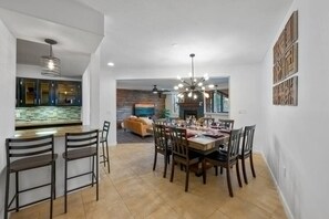 Ein Essbereich mit Holztisch und -stühlen, eine Küche im Hintergrund und ein Wohnzimmer mit Kamin.