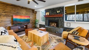 A living room with a stone fireplace, wooden walls, a television, and a ceiling fan. - Mountain View - Rooftop Patio - Theater - Games (Gatlinburg)