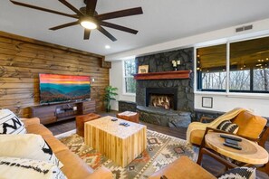 Ein Wohnzimmer mit Kamin aus Stein, Holzwänden, einem Fernseher und einem Deckenventilator.