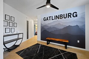 Ein Flur mit Wandbild von Bergen, Deckenventilator, gerahmten Zertifikaten, einer Bank und einem Schreibtisch mit Stuhl.