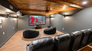 A home theater room with a wooden ceiling, black leather seating, and a large flat-screen TV. - Mountain View - Rooftop Patio - Theater - Games (Gatlinburg)