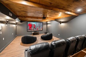 Ein Heimkino mit Holzboden, schwarzen Ledersesseln und einem großen Flachbildfernseher.