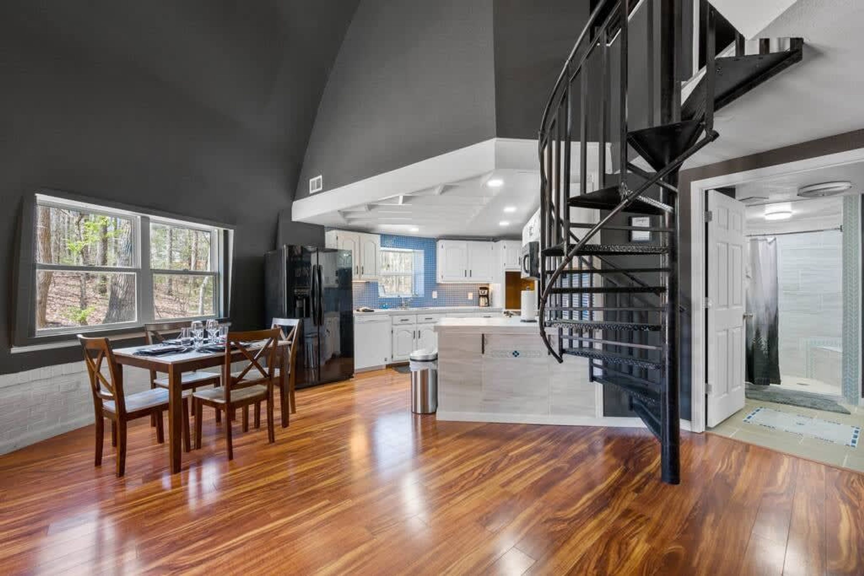 A spacious kitchen with a central island, a dining area with a wooden table and chairs, and a black spiral staircase.