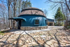 Un bâtiment bleu, en forme de dôme, avec des fondations en pierre, entouré d’une zone pavée de pierres et d’arbres.