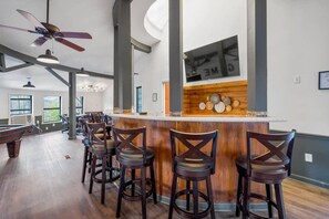 Un espace bar avec des tabourets en bois, un comptoir et un ventilateur de plafond.
