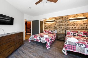 Ein Schlafzimmer mit zwei Betten, einer Holzkommode, einem Flachbildfernseher und einer Steinwand.