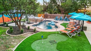 Un giardino sul retro con piscina, lettini e un campo da golf.