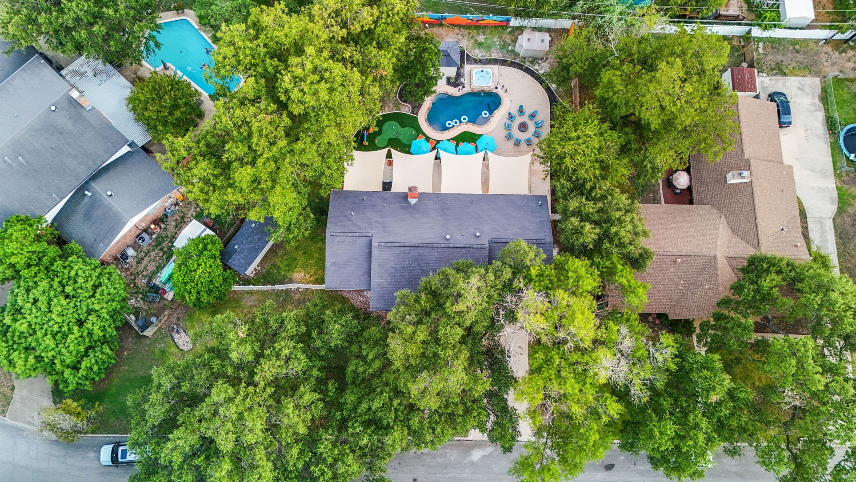 An aerial view of a residential area with a swimming pool, a hot tub, and a covered patio area.