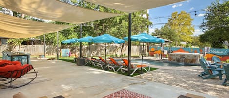 An outdoor patio area with lounge chairs, umbrellas, and a pool.