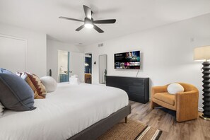 A modern bedroom with a bed, a TV mounted on the wall, a ceiling fan, and a side table with a lamp. - Resort Style Backyard Pool Putt Putt Hot Tub (San Antonio)