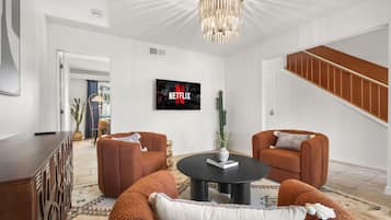 Ein modernes Wohnzimmer mit einem an der Wand befestigten Flachbildfernseher, zwei braunen Sofas, einem Couchtisch und einer Treppe, die zu einer oberen Ebene führt.