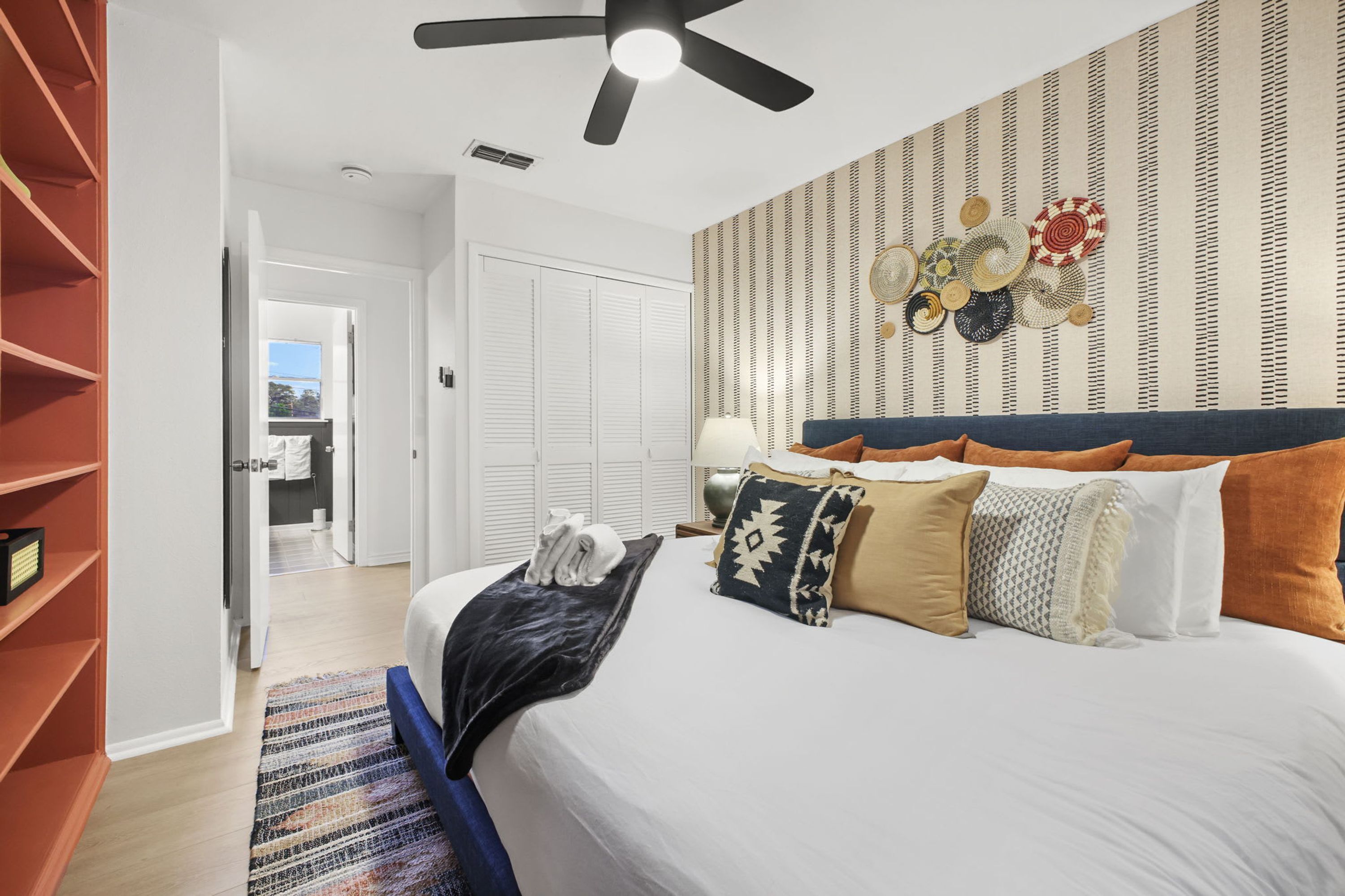A hotel room with a bed, a ceiling fan, a patterned wall, and a view of the outside.