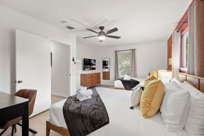 Ein Hotelzimmer mit einem Bett, einem Schreibtisch, einem Stuhl, einem Deckenventilator, einem Fernseher und einem Fenster mit Jalousien.