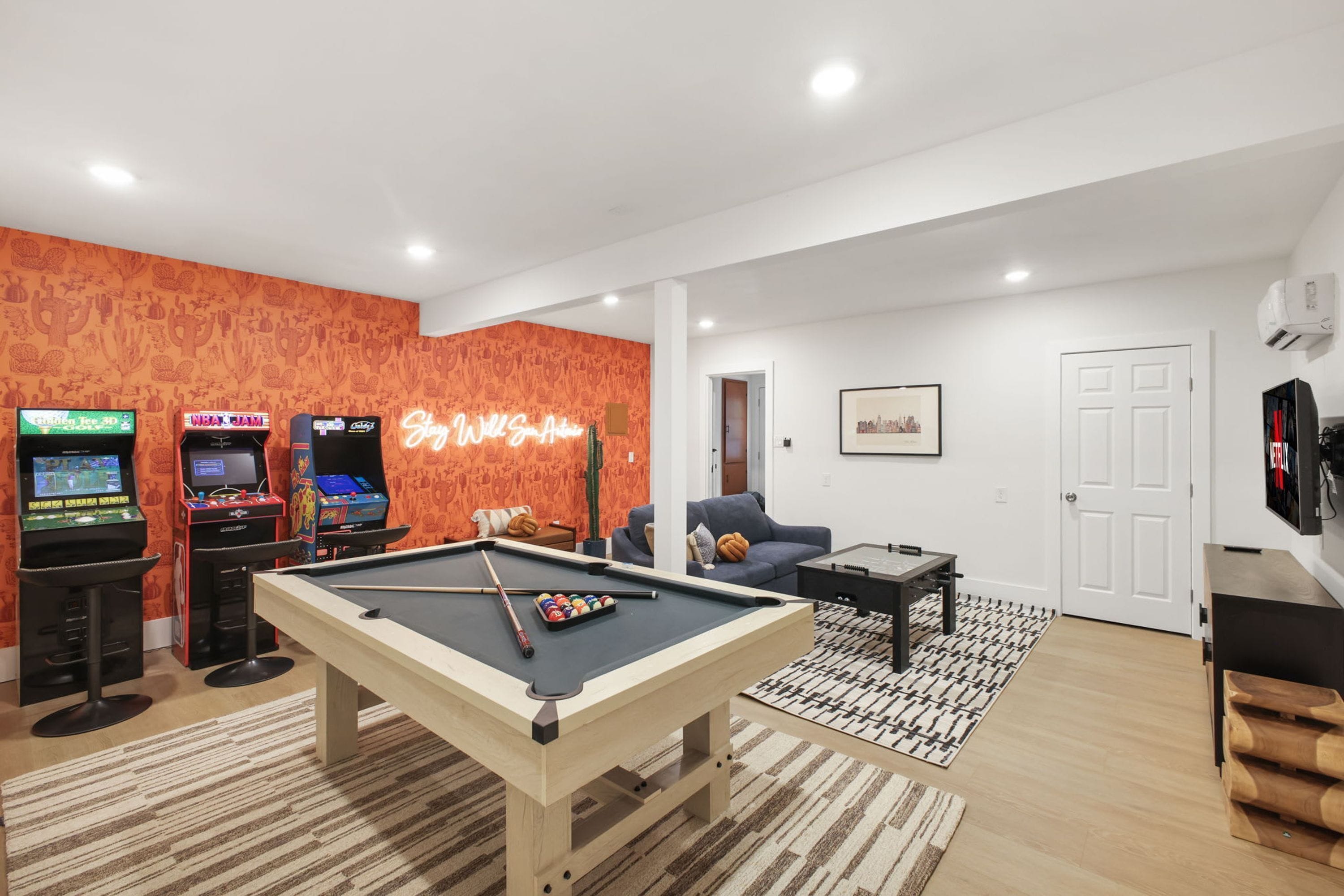 A living room with a pool table, a sofa, and arcade games.