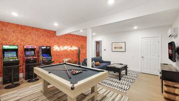 Ein Wohnzimmer mit Billardtisch, einer Couch und Spielautomaten.