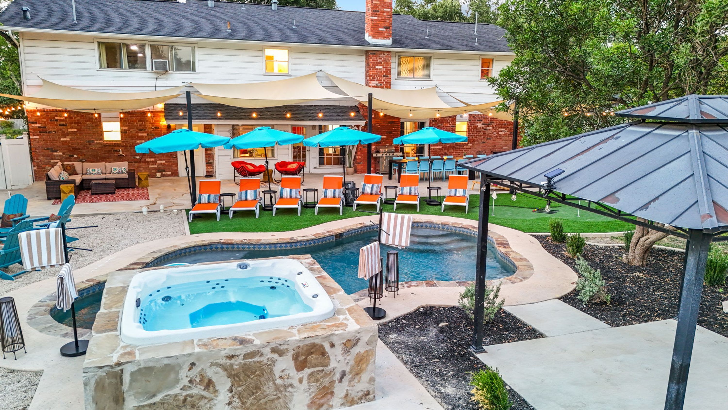 A backyard with a hot tub, lounge chairs, and umbrellas.