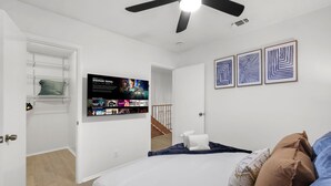 Una camera da letto con un letto, una ventola a soffitto, una TV a parete e opere d'arte sopra il letto.