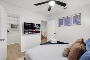 A bedroom with a bed, a ceiling fan, a TV mounted on the wall, and artwork above the bed. - Resort Style Backyard Pool Putt Putt Hot Tub (San Antonio)