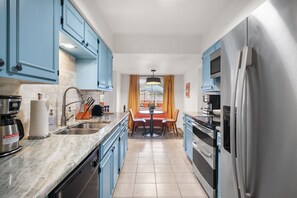 A modern kitchen with blue cabinets, stainless steel appliances, and a dining area with a table and chairs. - Resort Style Backyard Pool Putt Putt Hot Tub (San Antonio)