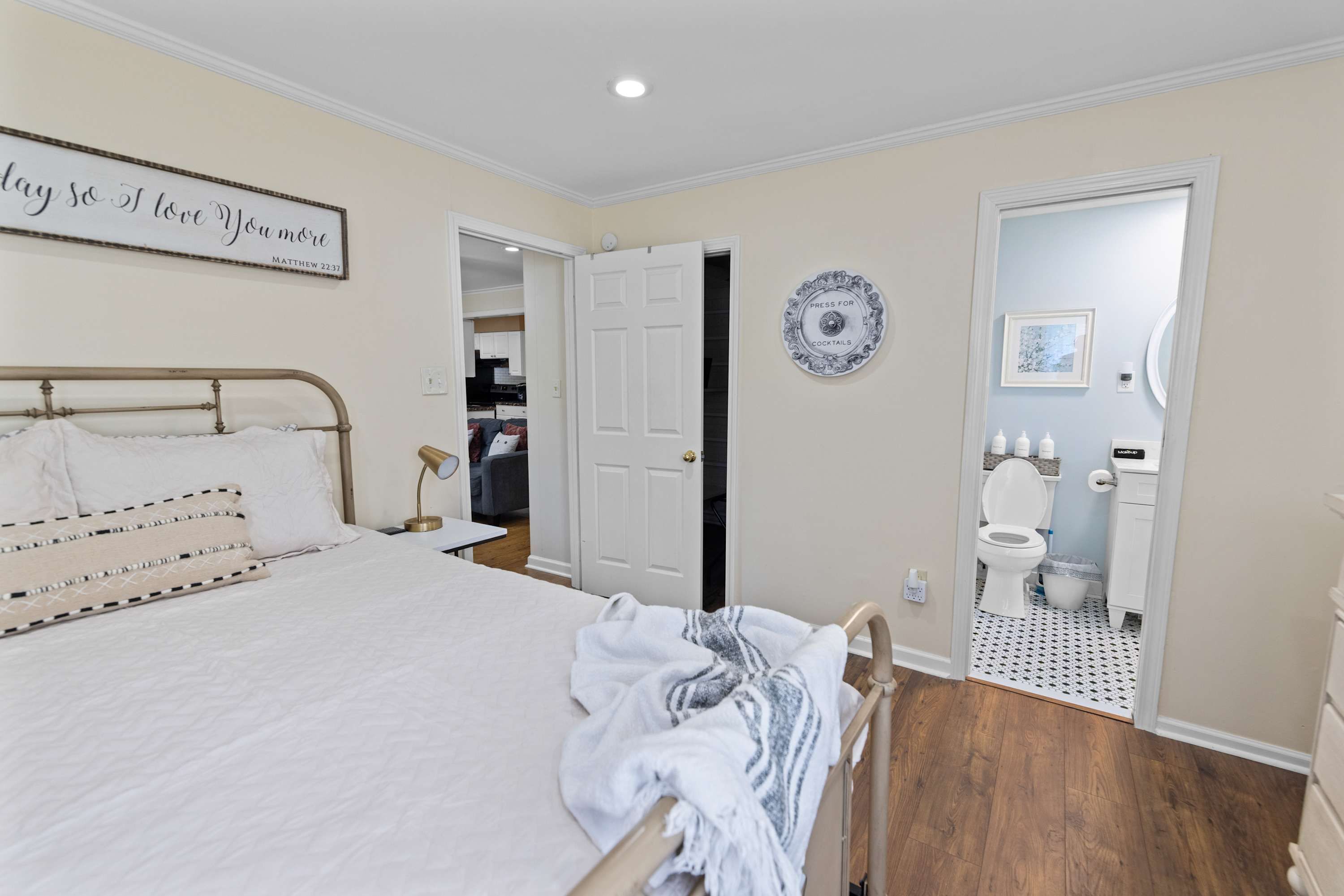 A bedroom with a bed, a bedside table, a wall-mounted clock, and a door leading to a bathroom.