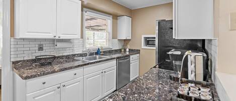 A kitchen with white cabinets, a granite countertop, a stainless steel sink, and a microwave.