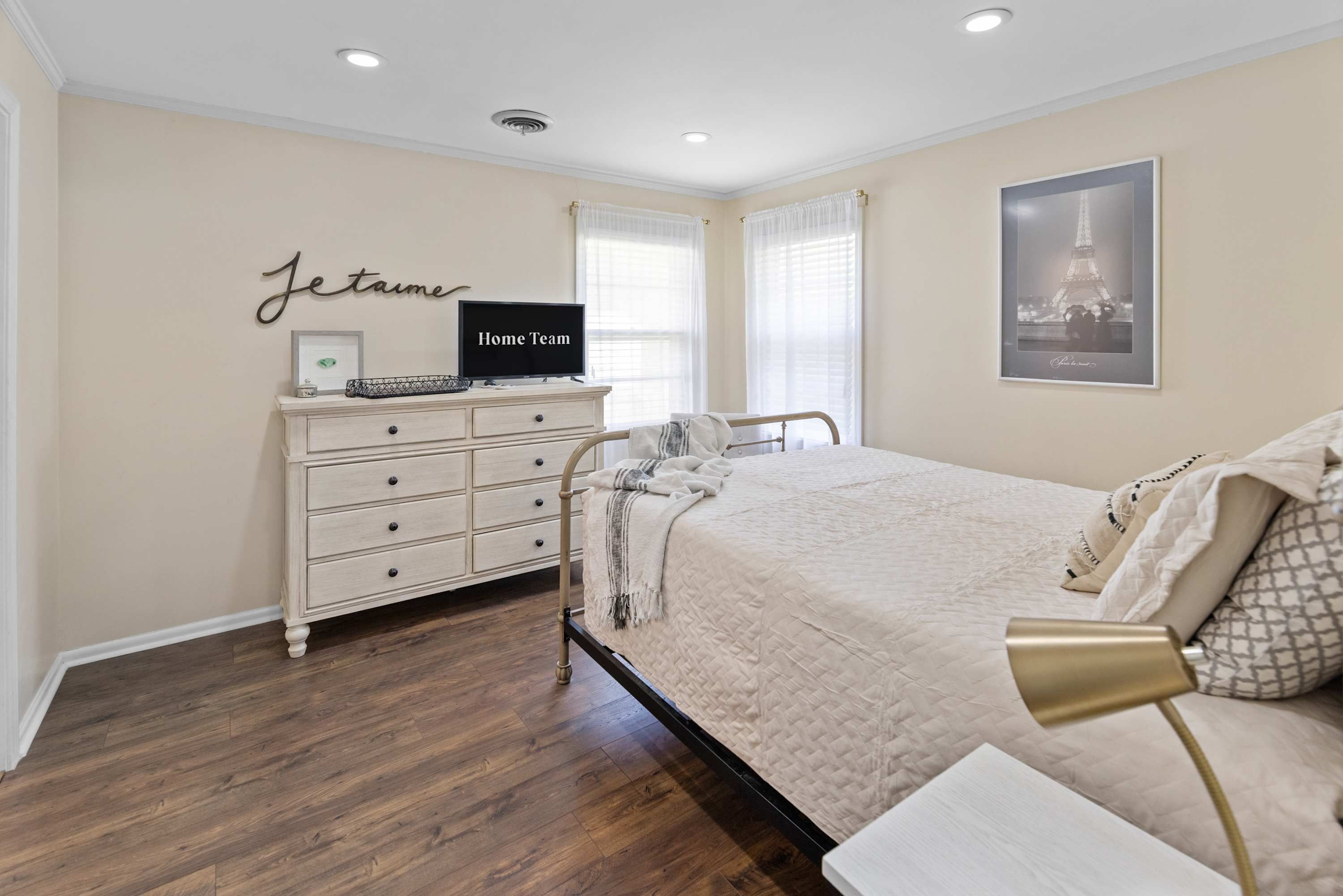 A bedroom with a bed, a dresser, a television, and a framed picture of the Eiffel Tower.