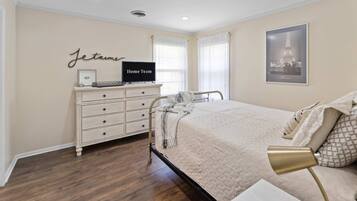 A bedroom with a bed, a dresser, a television, and a framed picture of the Eiffel Tower.