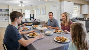 A family dining in a modern kitchen with white cabinets, a dining table, and a ceiling fan.