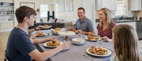A family dining in a modern kitchen with white cabinets, a dining table, and a ceiling fan.