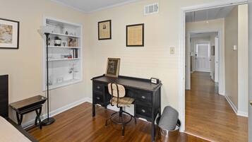 A room with a wooden floor, a desk with a chair, a bookshelf, and a framed picture on the wall.