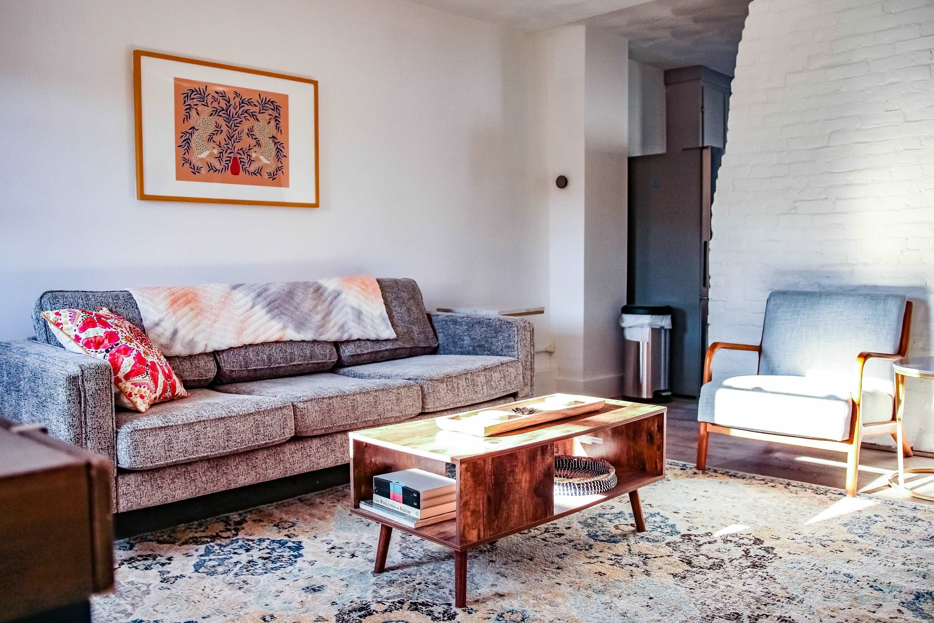 Een woonkamer met een grijze bank, een bijzettafeltje, een stoel en een lijst met kunstwerk aan de muur.