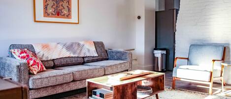 A living room with a grey sofa, a coffee table, a chair, and a framed artwork on the wall.