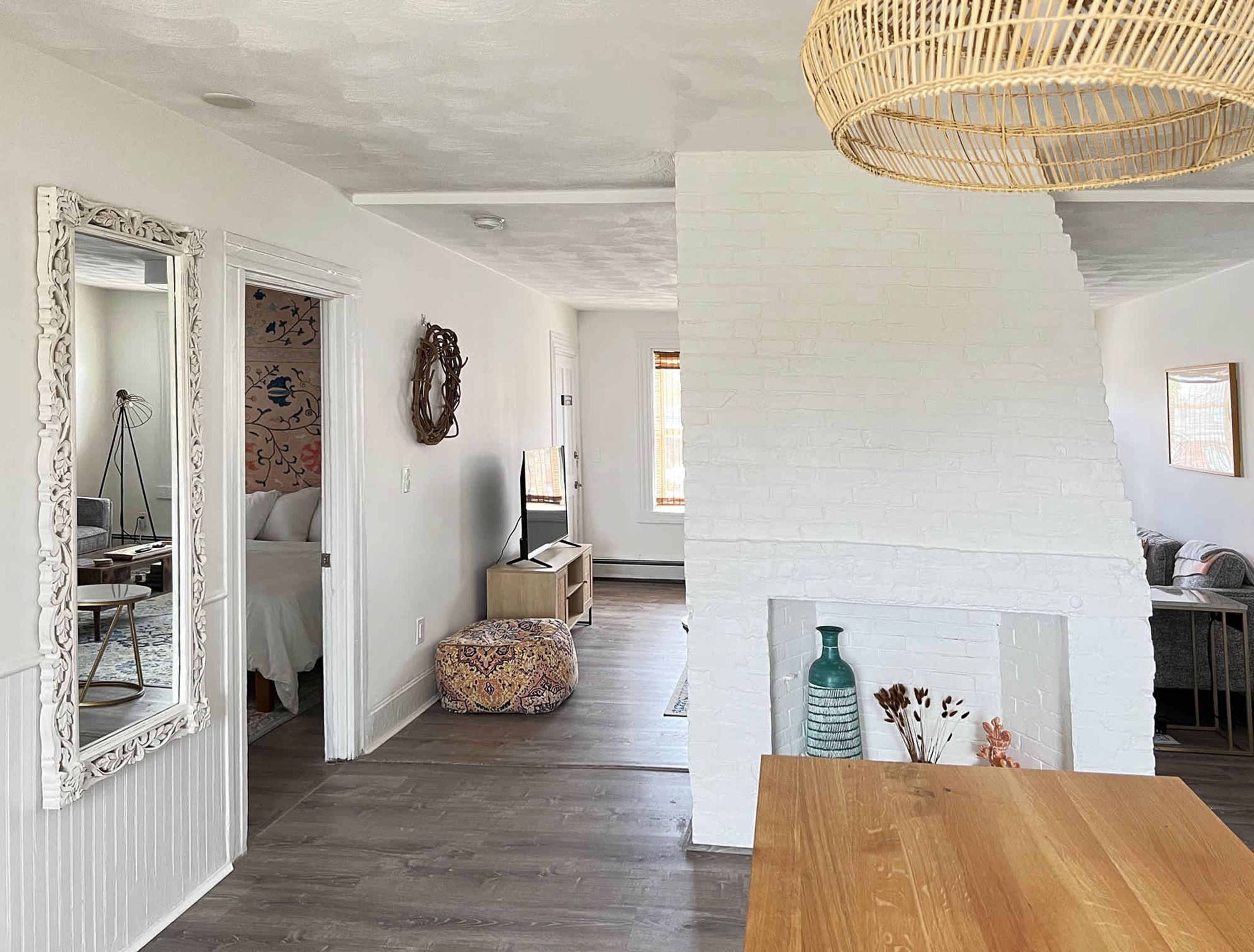 Un'ampia zona giorno con camino in mattoni bianchi, un tavolo da pranzo in legno e una lampada a soffitto in rattan.