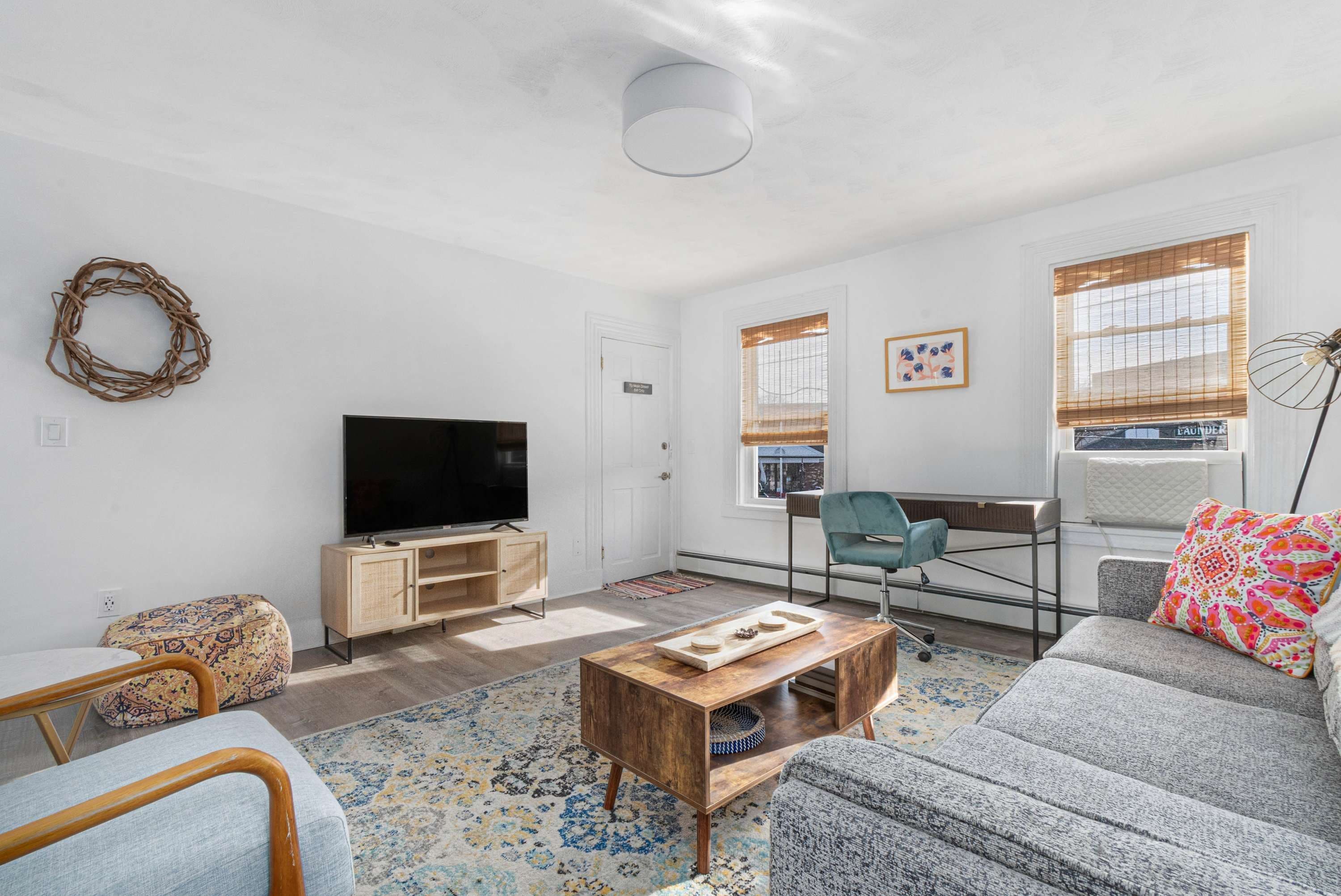 A modern living room with a flat-screen TV, a wooden coffee table, a sofa, a chair, and a patterned rug.