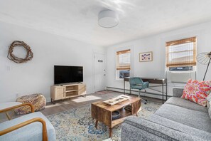 A modern living room with a flat-screen TV, a wooden coffee table, a sofa, a chair, and a patterned rug.