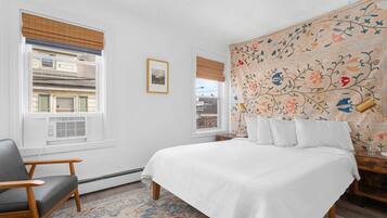 A bedroom with a bed, a chair, a window with blinds, and a patterned wall.