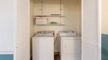 A laundry room with two stacked washers and dryers, a shelf with a box, and a hanging rack.